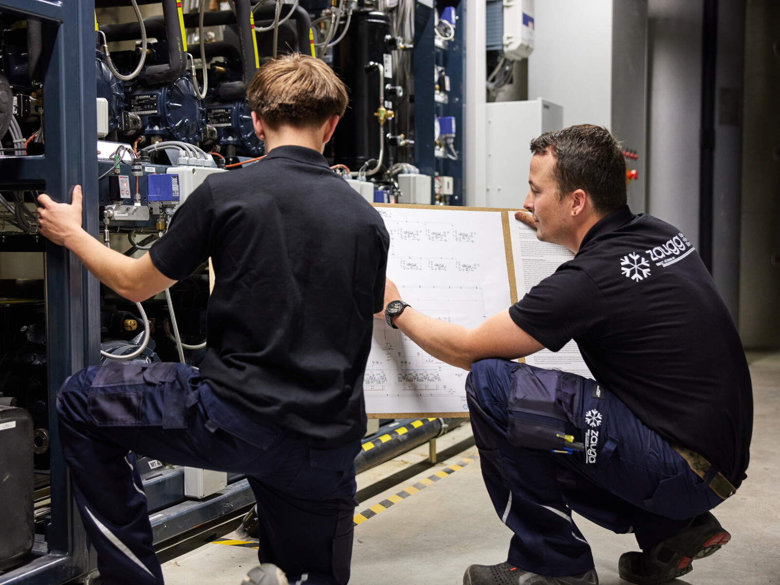 Ein Kältesystemmonteur erklärt einem Lernenden das R+I Schema einer CO2 Kälteanlage