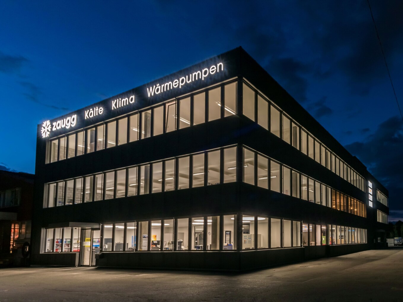 Beleuchtetes Firmengebäude der Zaugg AG bei Nacht – Spezialist für Kälte, Klima und Wärmepumpen.